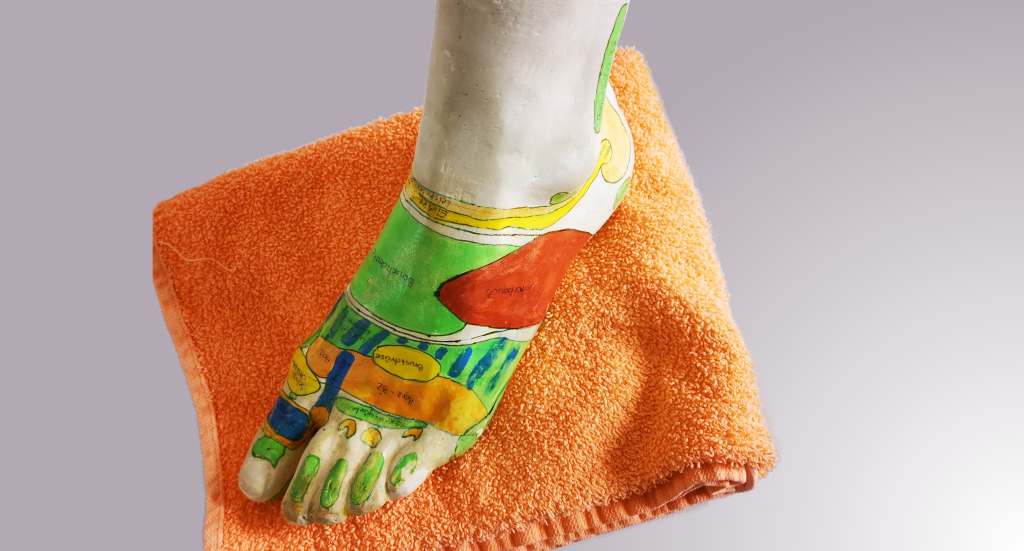 Die Fußreflexzonen aanhand eines Gipsmodells, auf einem orangen Frotteehandtuch