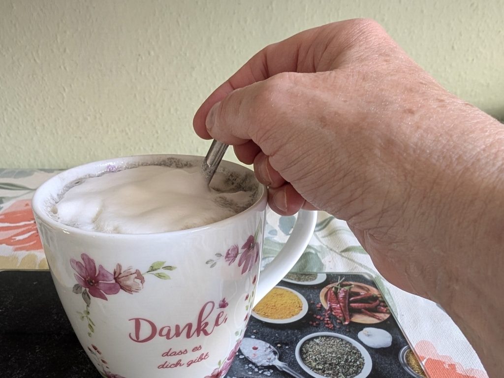 Zeit ohne Aufgabe Eine Hand am Frühstückstisch, die den Kaffee in einer großen Tasse umrührt